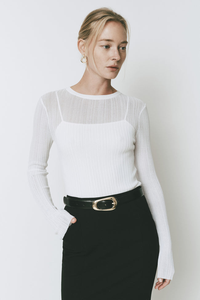Ruesophie Iris white sheer ribbed knit long-sleeve sweater on a model with black tailored trousers.