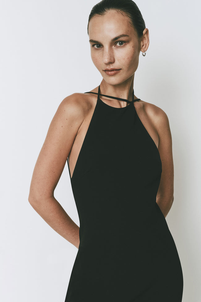 Black Opera Dress with halter neck, midi length, and open back. Featuring a model.