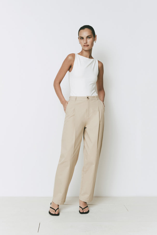 White Ruesophie Plage high-neck sleeveless bodysuit, modeled with beige pleated trousers. Lightweight, soft fit.