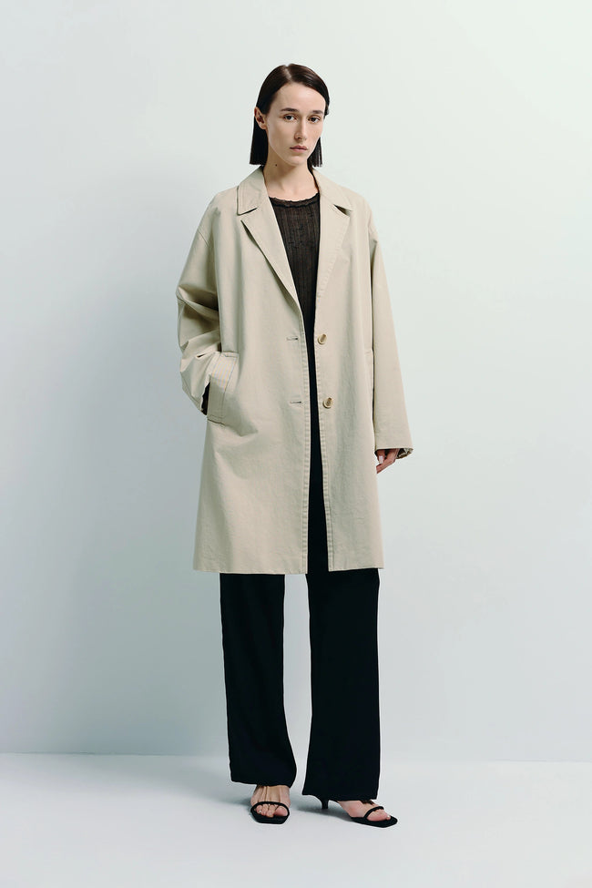 Dune Cotton Twill Coat in light beige, oversized fit. Model wearing black pants and sandals.