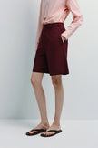 Maroon linen Bermuda shorts with pink shirt and brown flip-flops. Versatile shorts for warm weather.
