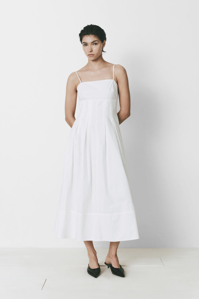 White Virginie dress with square neckline and adjustable straps, paired with black mules, minimalist and chic