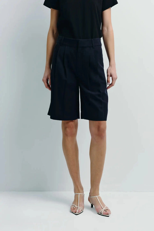 Navy high-rise Bermuda shorts in lyocell and linen, styled with a black tee for refined warm-weather wear