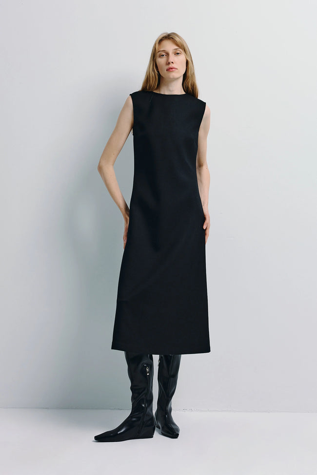 Black A-line midi dress with boatneck. Minimal, refined style. Paired with black leather boots.