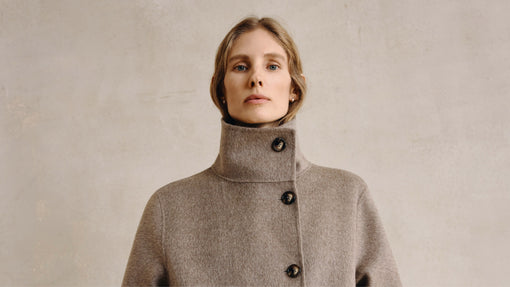 A model poses in a long, light brown coat with a high, buttoned collar, her hands in her pockets