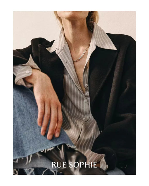Close-up of a striped shirt layered under a black coat, paired with denim jeans