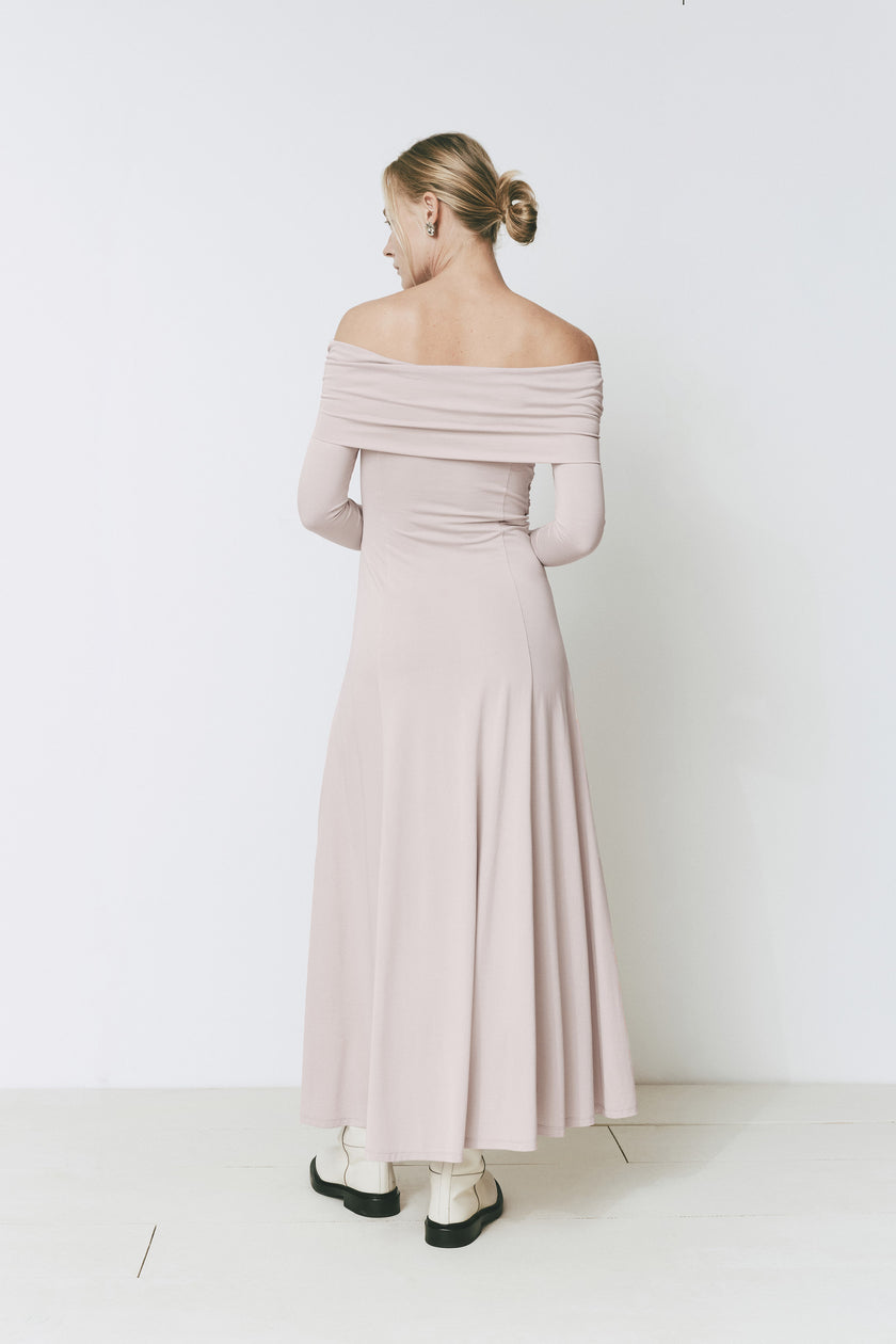 Giverny Dress in light pink, featuring an off-the-shoulder design and maxi length. Woman wearing boots.