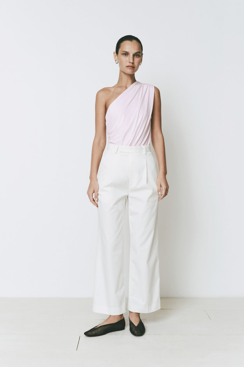 Perle bodysuit in pink with one shoulder design and ruched detail, paired with white trousers