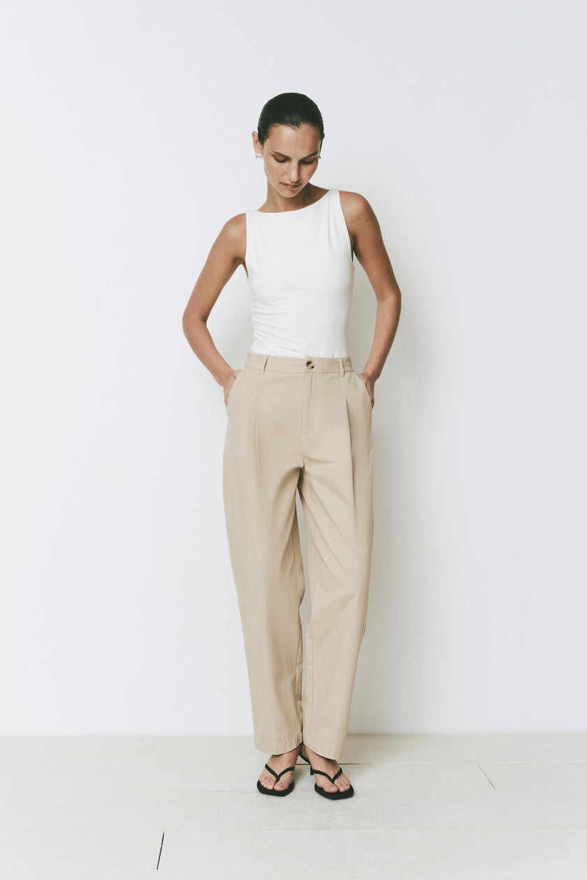 White Ruesophie Plage high-neck sleeveless bodysuit, lightweight & soft, paired with beige pleated trousers.