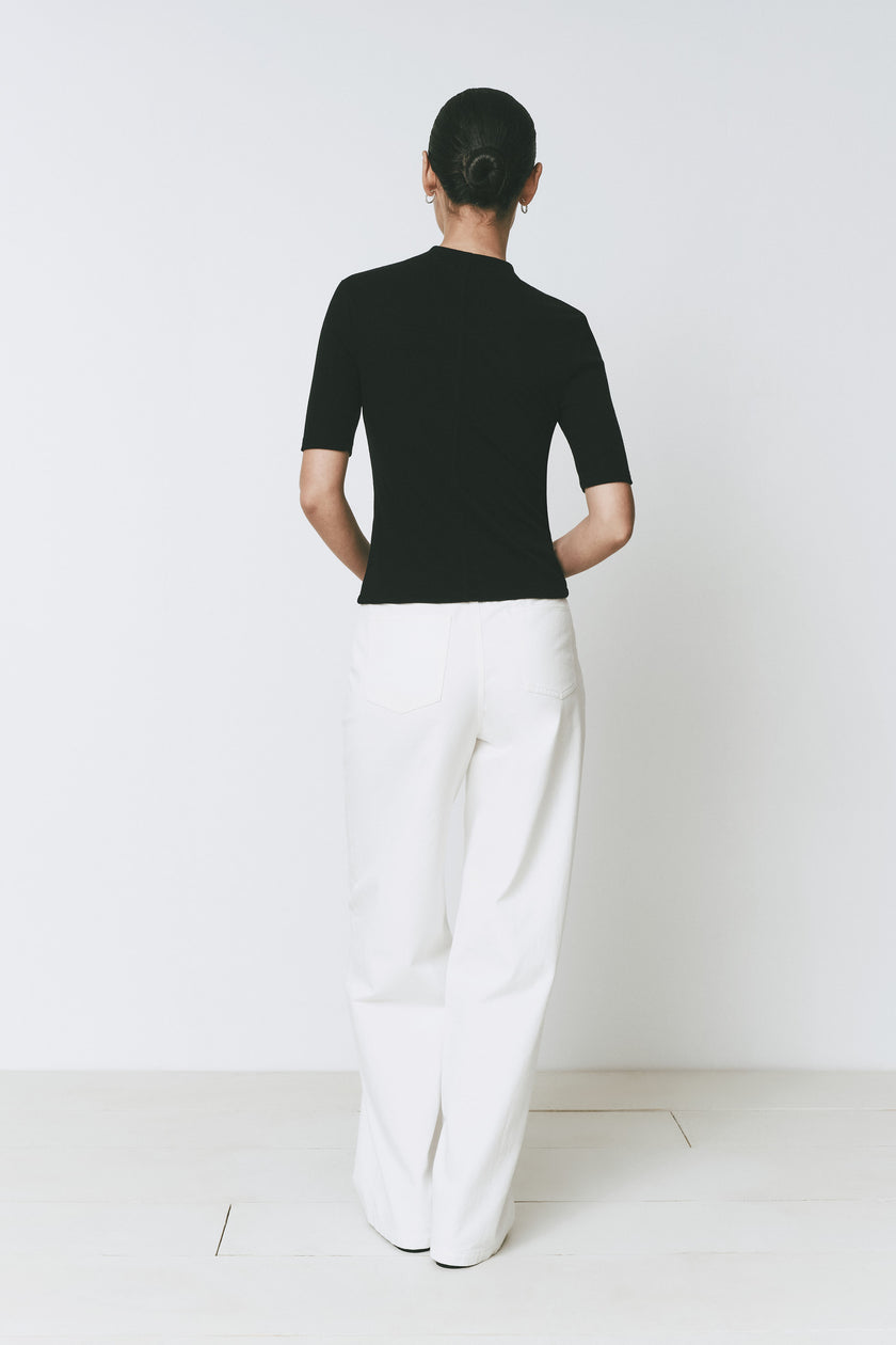 Rear view of Ruesophie's black Chabot mock neck top with quarter sleeves, styled with white trousers.
