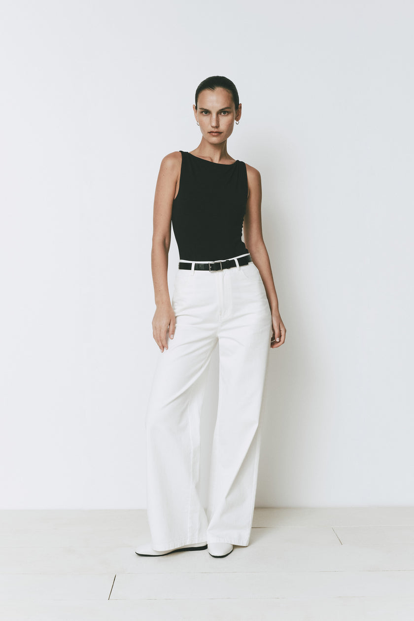 Black high-neck sleeveless Plage Bodysuit for women, shown with white flowy pants and a black belt.
