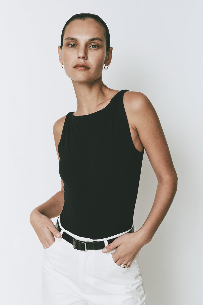 Black Plage Bodysuit for women, featuring a high-neck and sleeveless design, styled with white pants.