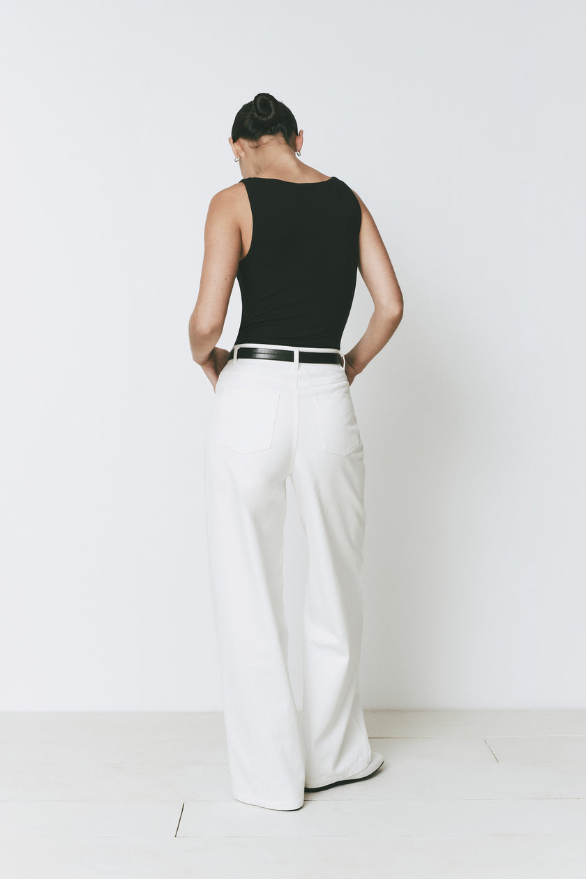 Minimalist black sleeveless Plage Bodysuit for women, high-neck design, complemented by white pants and black belt.