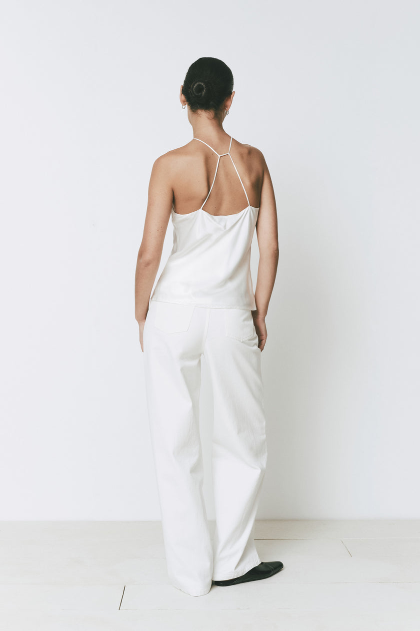 Back view of woman in white Arc Top halter neck top and wide leg white pants. Minimalist style.