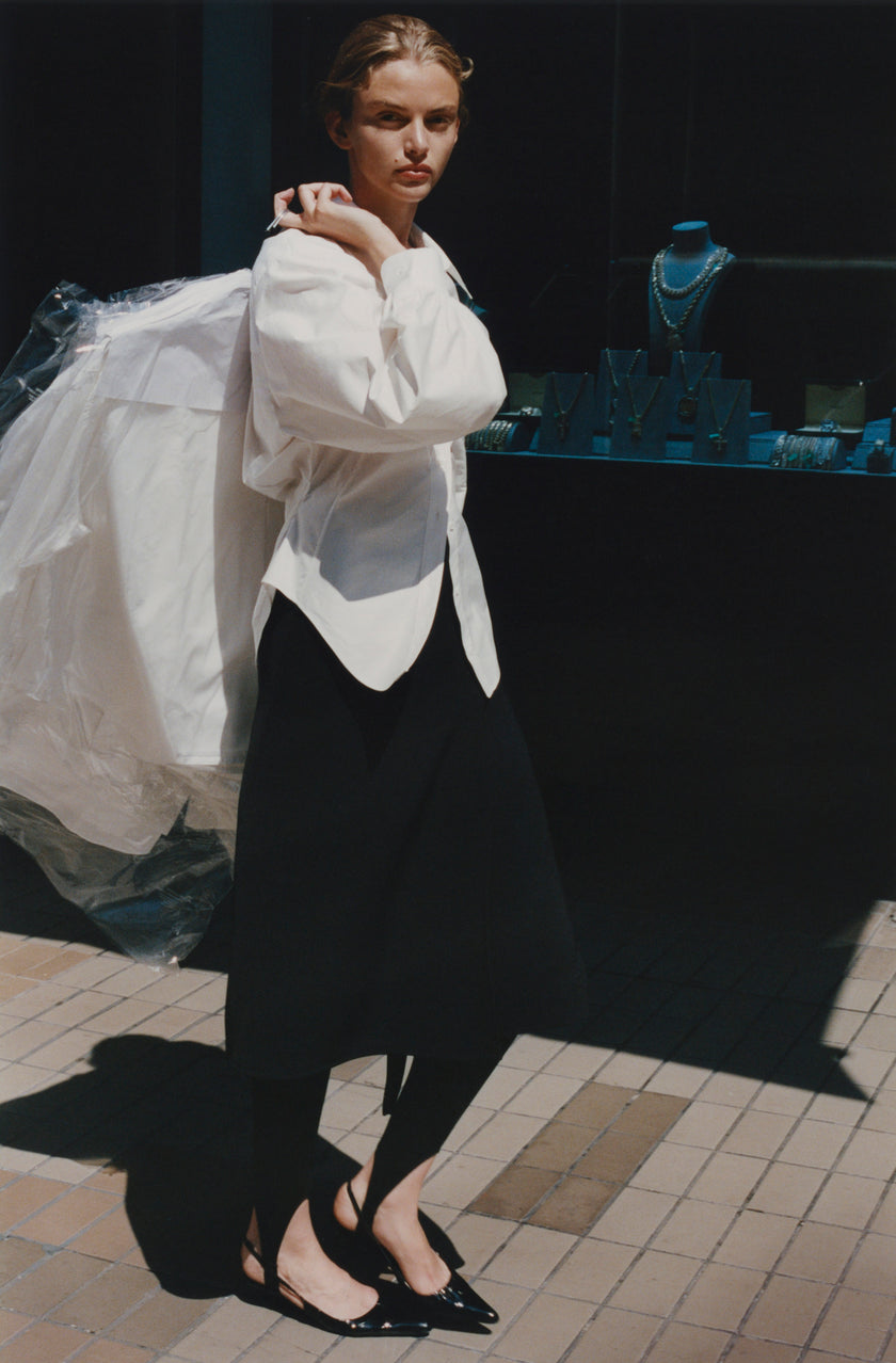 Woman in black Belmont Wrap Skirt and white shirt, black flats. Sophisticated daytime or evening wear.