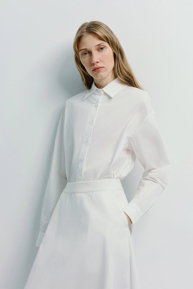 Woman wearing Alda button-down shirt made of 100% cotton. White shirt with button details.