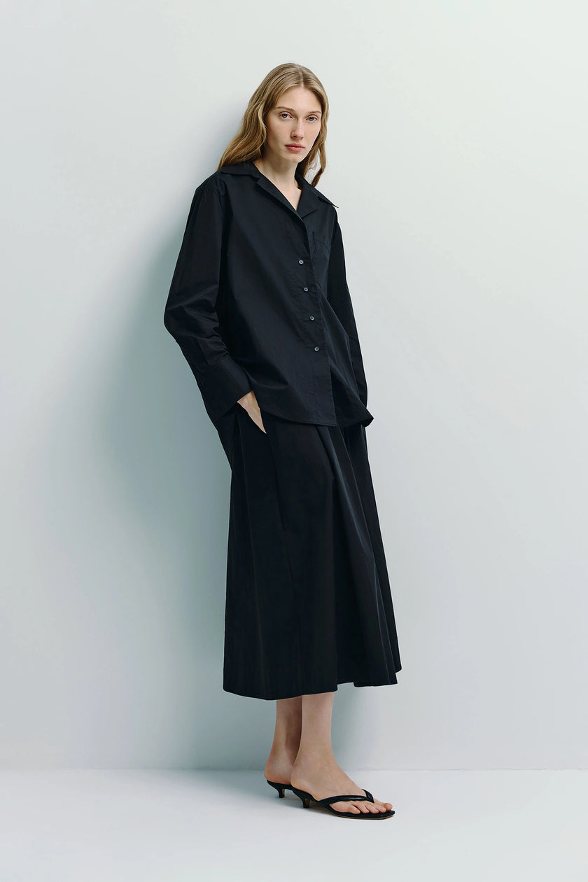 Black poplin midi skirt styled with a black shirt. Featured on a model, showcasing the skirt's flowy silhouette.