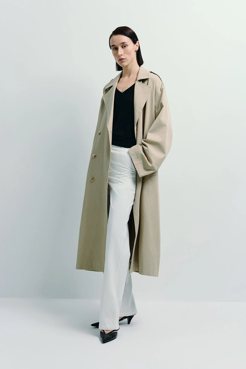 Beige Balham Trench Coat from Rue Sophie, double-breasted design, woman in black top and white pants.
