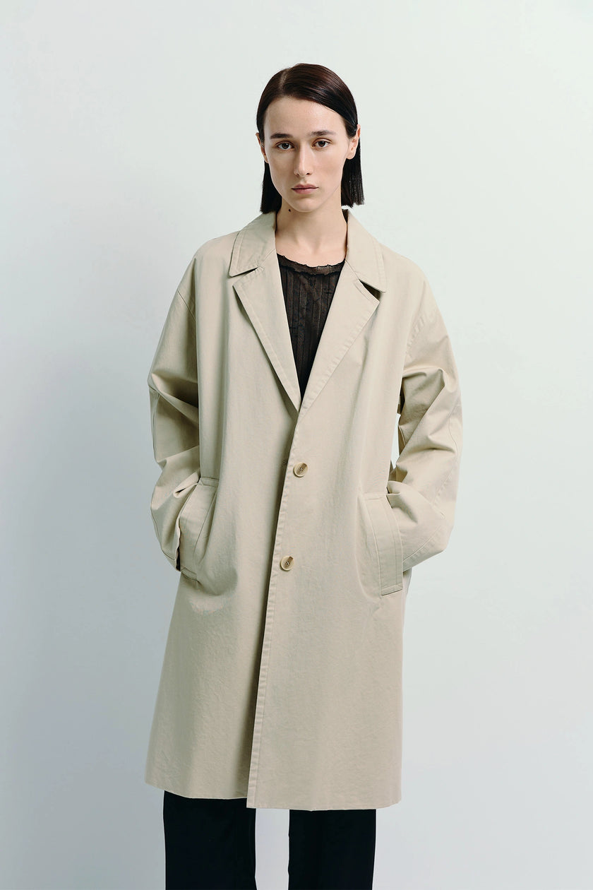Oversized Dune Cotton Twill Coat in light beige, model wearing black outfit, a timeless outerwear piece.