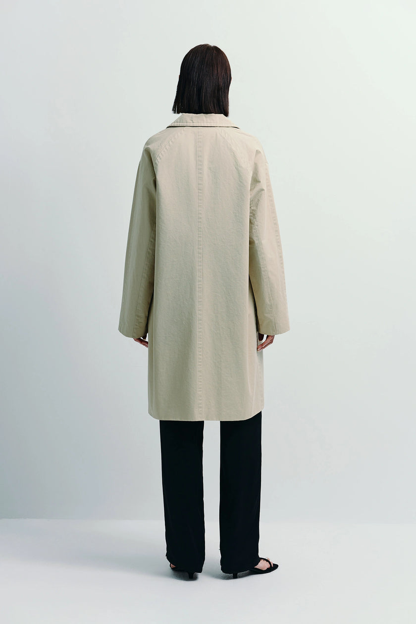 Dune Cotton Twill Coat in light beige, oversized fit, with black pants. Timeless outerwear.