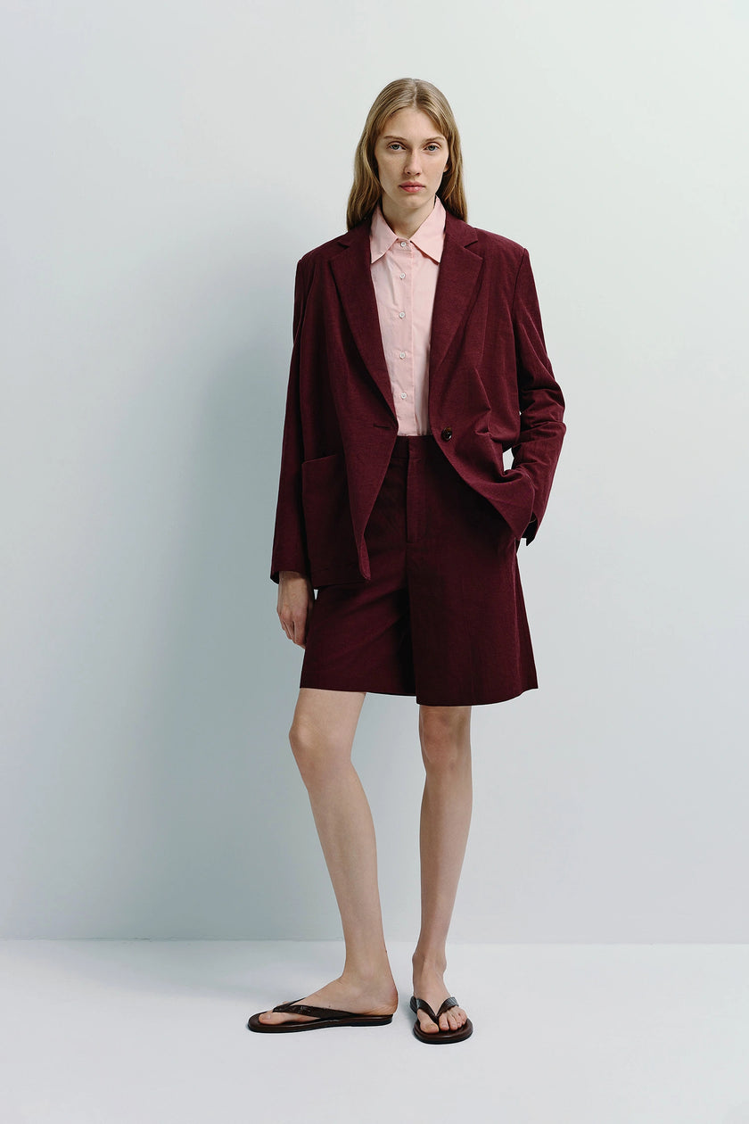 Woman wearing maroon linen Bermuda shorts suit with a pink shirt. Versatile style for warmer weather.
