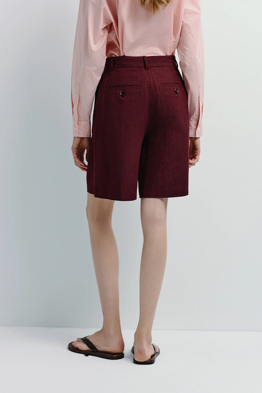 Woman in burgundy linen Bermuda shorts and pink shirt. Versatile shorts for warmer weather.