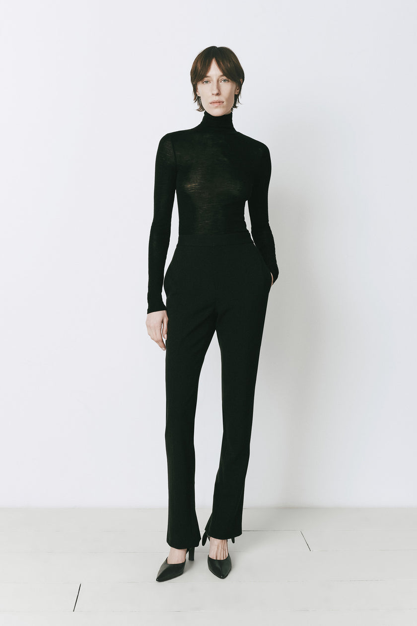 Black Baïa Slit Hem Pant, polyester-rayon blend, styled with a black turtleneck for a minimalist, chic look.
