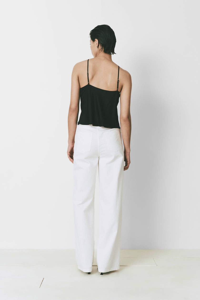 Yvoire Top in black with adjustable straps, paired with white wide-leg pants. Modern style.