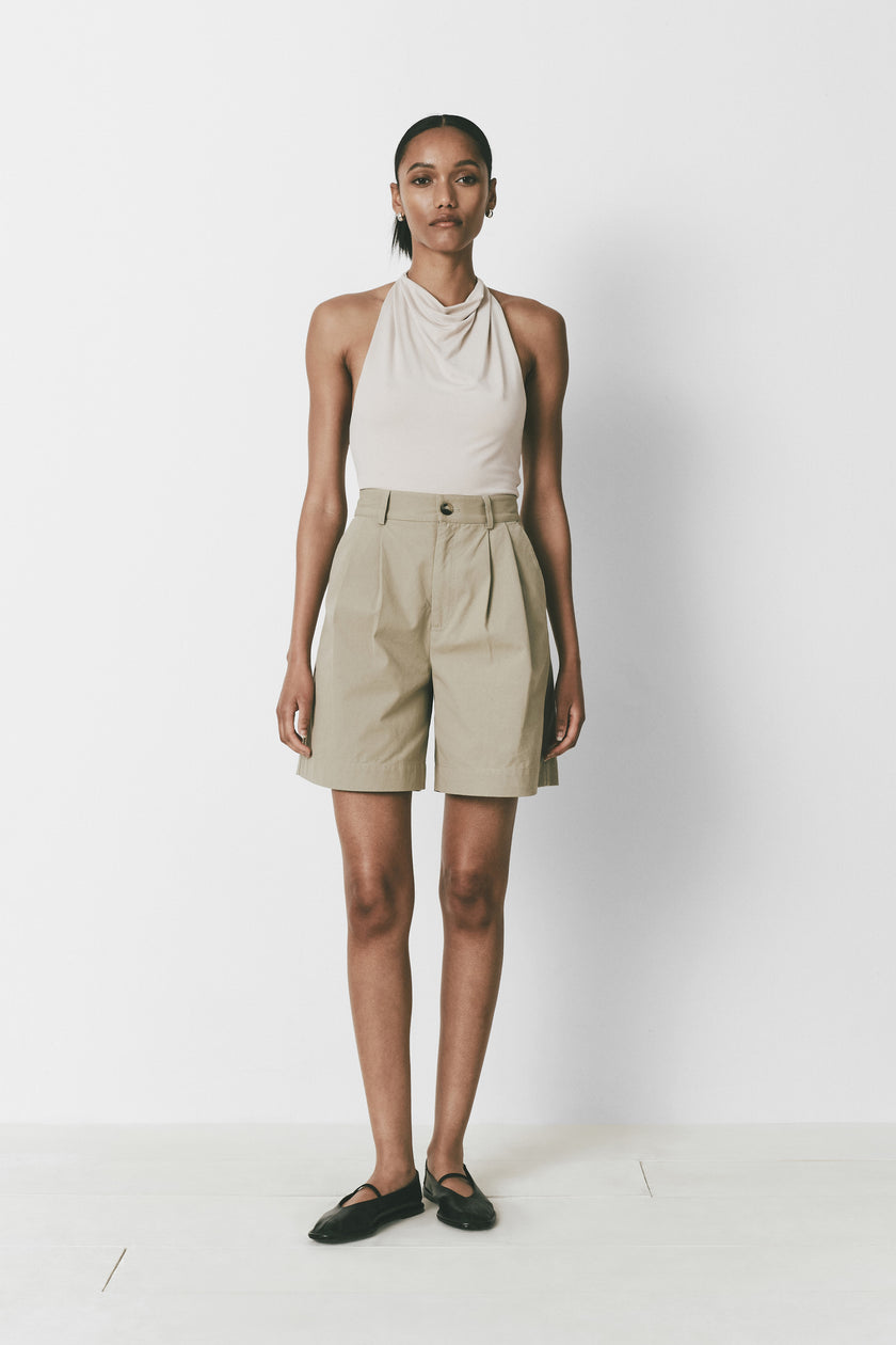 Alain Shorts in khaki. Mid-thigh length shorts, featuring pleat front, button closure. Paired with neutral halter top.