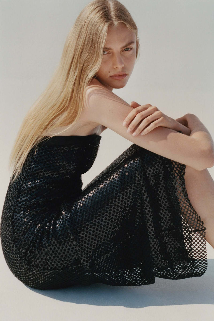 Black sequin crochet mesh dress, strapless design, ideal for festive occasions. Model wearing a stylish dress.