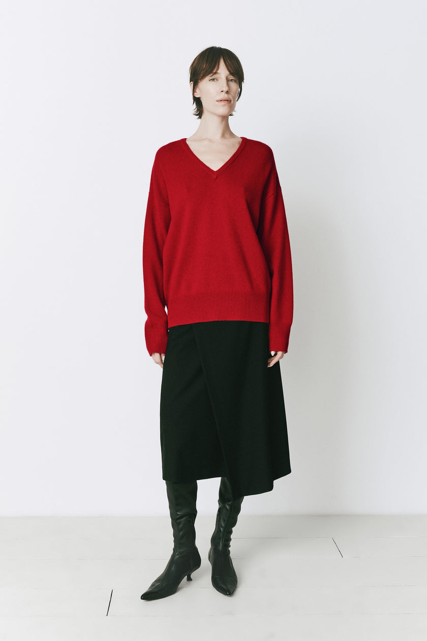 Ruesophie Coquelicot red V-neck sweater paired with black skirt and boots, fall layering look.