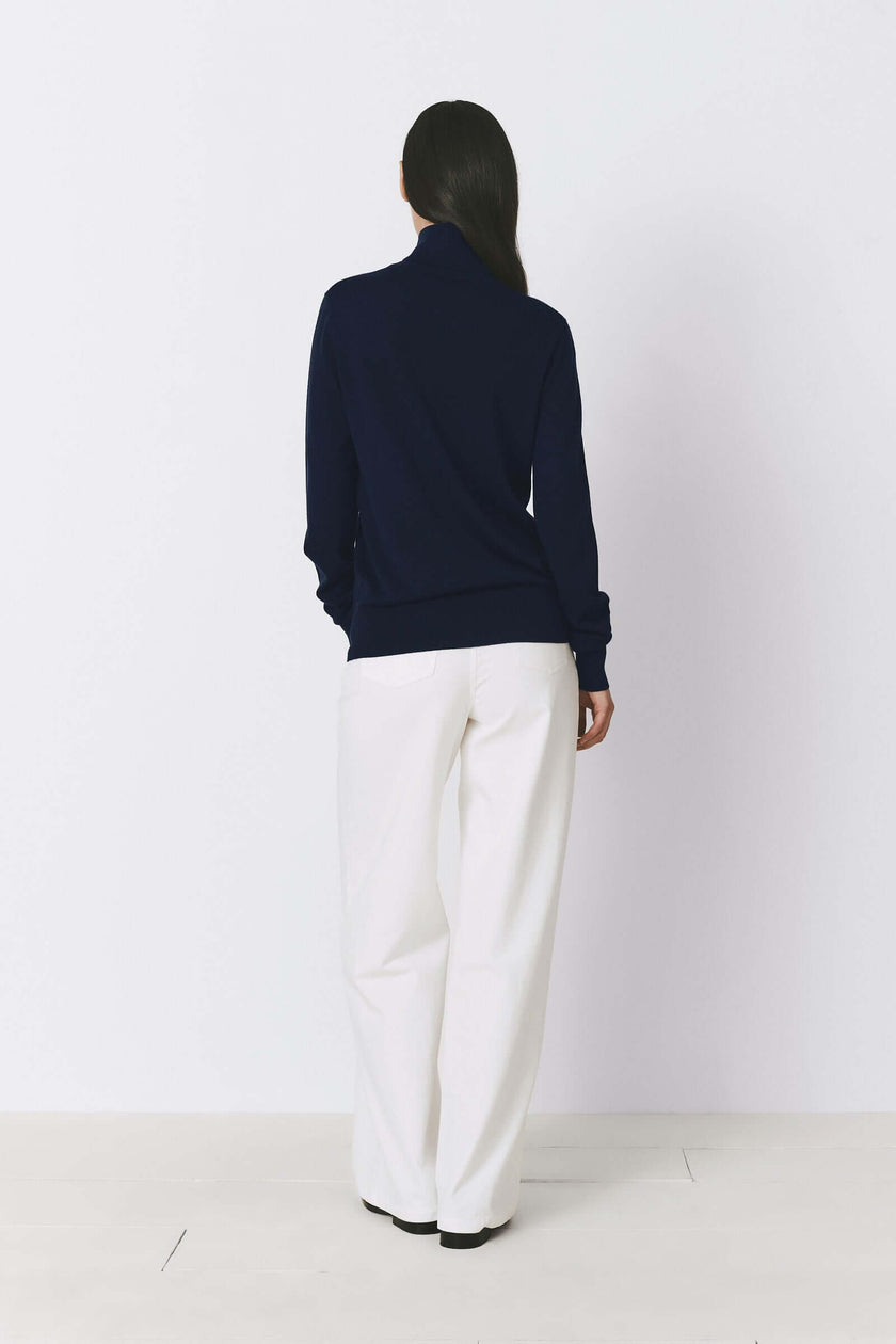 Navy blue Dion Wool & Silk Sweater, woman in a turtleneck sweater and white pants, back view.