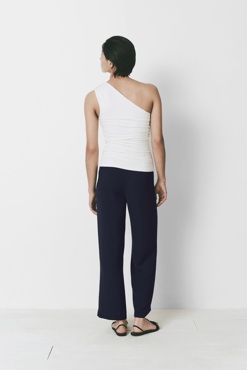 Rue Sophie Le Champ Top in white with one shoulder and soft fabric, paired with navy pants