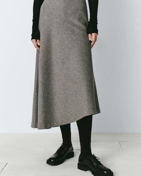 Grey wool asymmetric skirt with black top, tights, and leather shoes. Modern elegant cool-weather styling.