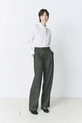 Model wearing pleated front straight leg trousers with an extended tab closure, styled with a white button-up shirt, showcasing a tailored fit and refined silhouette for a sophisticated, professional look.