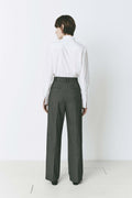 Model wearing pleated front straight leg trousers with an extended tab closure, styled with a white button-up shirt, showcasing a tailored fit and refined silhouette for a sophisticated, professional look.