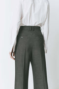 Model wearing pleated front straight leg trousers with an extended tab closure, styled with a white button-up shirt, showcasing a tailored fit and refined silhouette for a sophisticated, professional look.