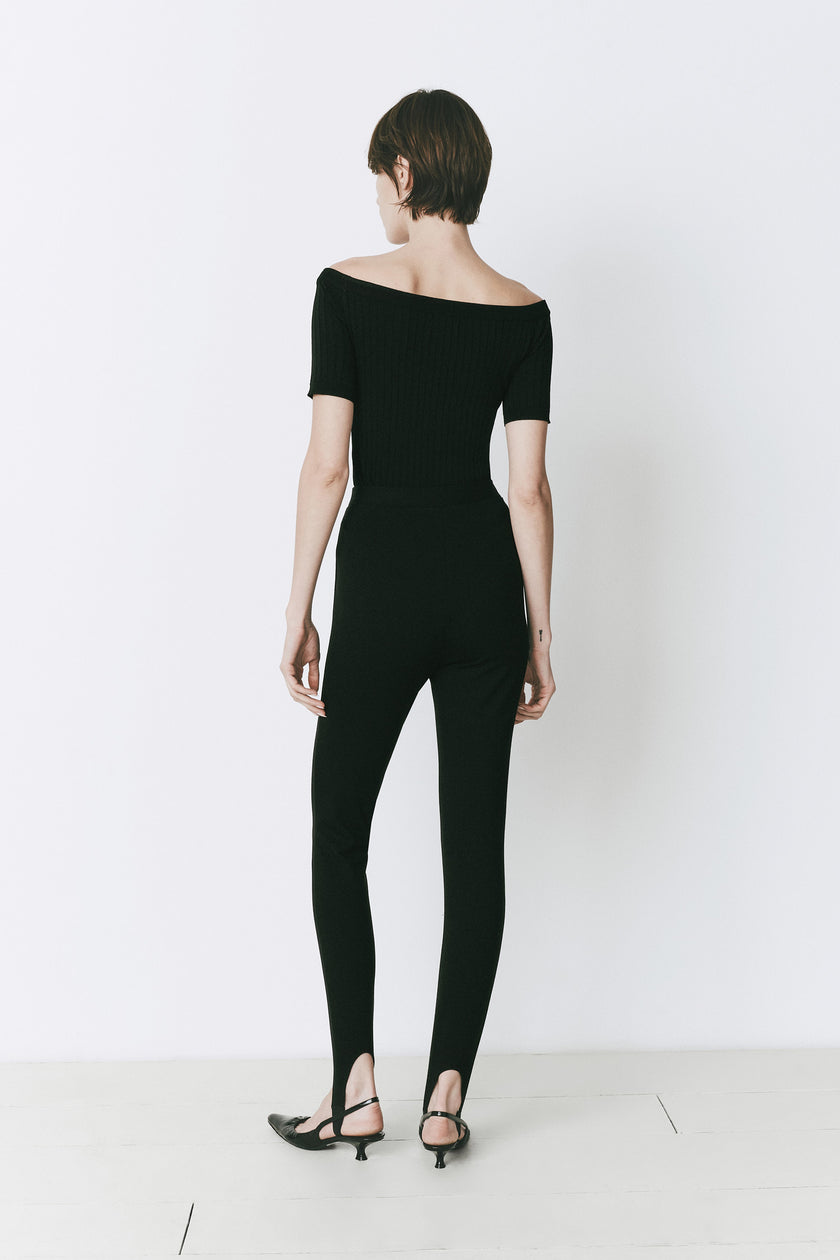 Black off-shoulder top and stirrup pants. Modern evening wear, minimalist style.