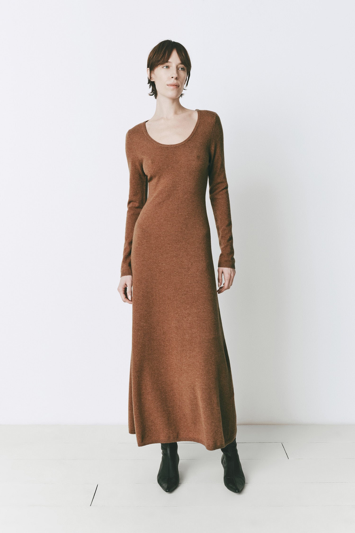 Model wearing the Mignet Sweater Dress, a long, oversized brown knit dress with a round neck and long sleeves