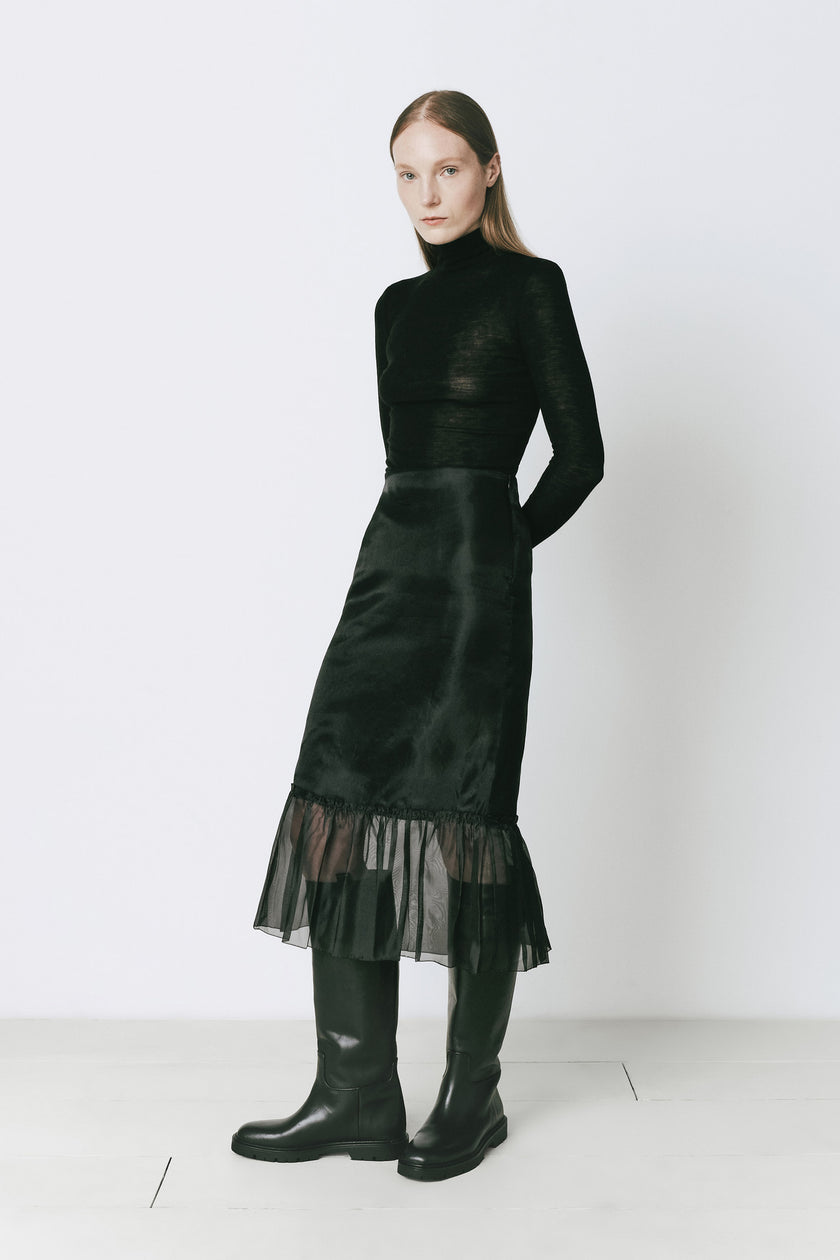Black midi skirt with organza peplum and turtleneck top, paired with knee-high boots, fall fashion.