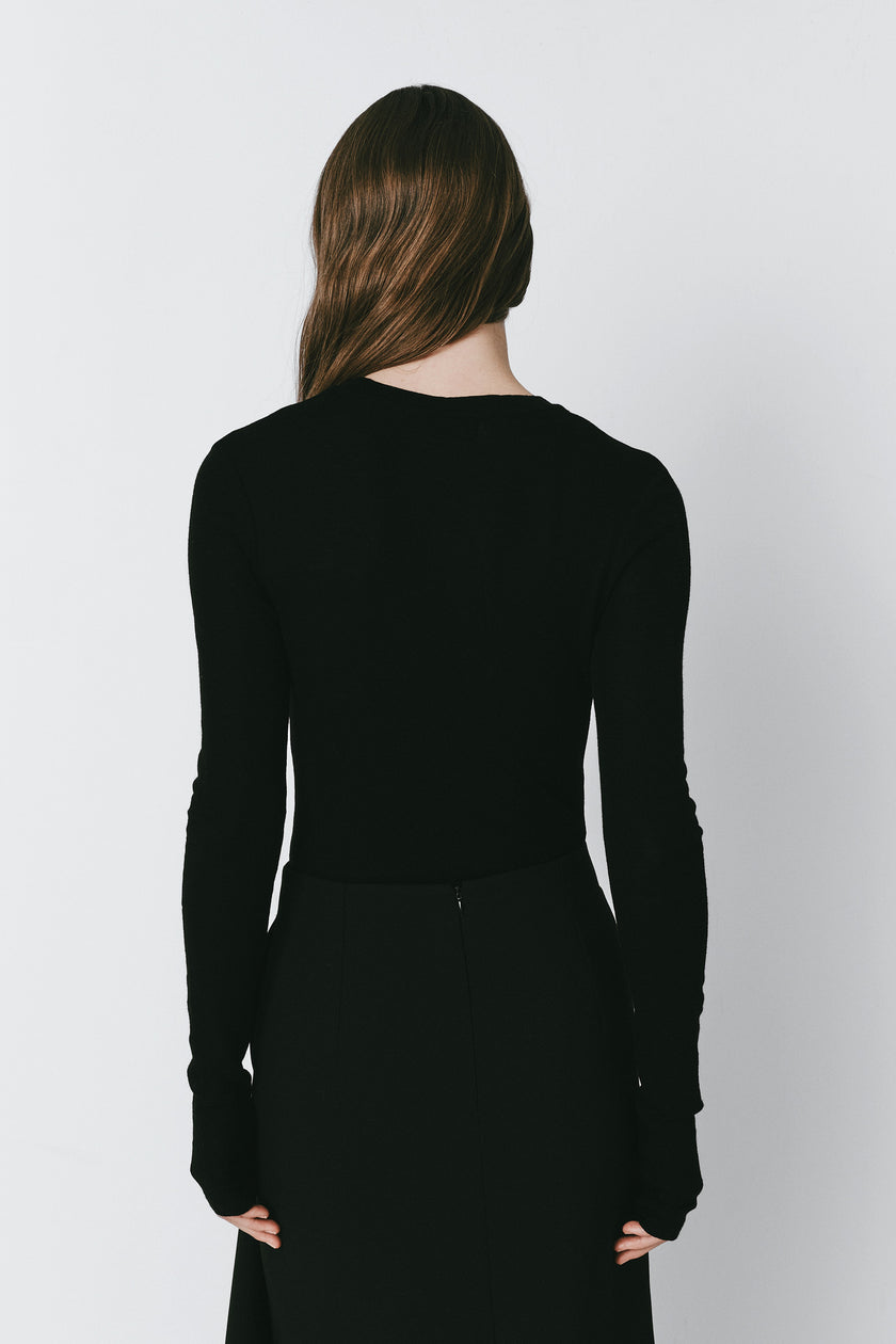 Oudine Sheer Wool Top in Black. Back view of a woman wearing a fitted, long-sleeved top with a matching skirt.