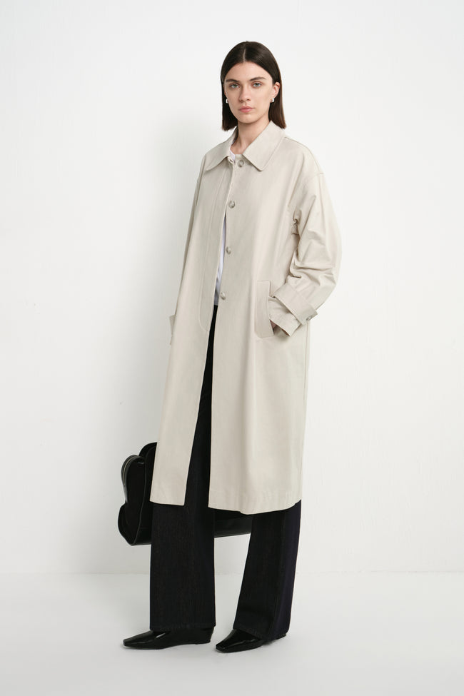 A model wearing the Rue Sophie Roche Oversized Jacket in cement, featuring a pointed collar, button-front closure, dropped shoulders, and a relaxed long silhouette, three-quarter front view.