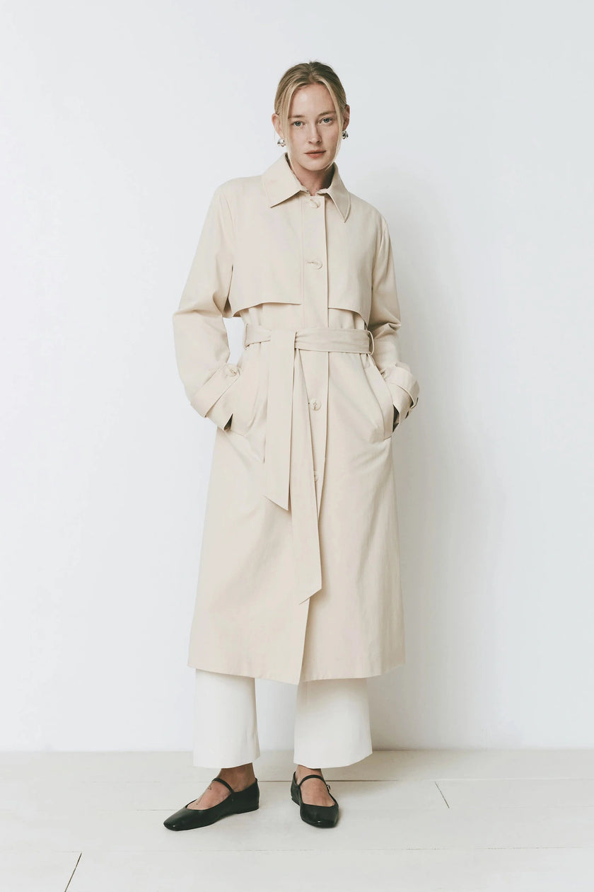 Cassis Trench Coat in beige, classic design with wide collar, adjustable belt and relaxed fit, featuring on a model.