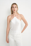 A blonde model wearing a white halter-neck camisole top and matching white trousers, standing against a plain white studio background.