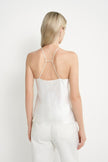 A woman shown from the back wearing a white satin camisole top with thin double straps and white pants, against a plain white studio background.