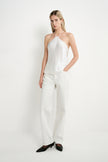 A woman modeling a white satin halter top and matching white wide-leg trousers, paired with black pointed-toe flats, against a clean white studio background.