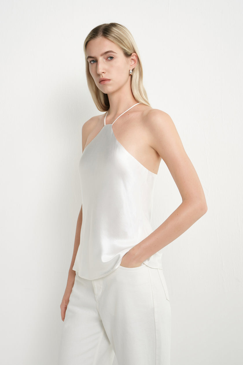 A blonde model wearing a white satin halter top and matching white trousers, standing against a plain white studio background.