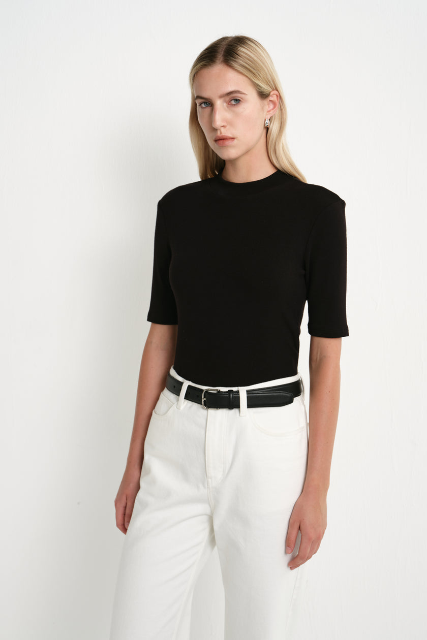 A model wearing the Rue Sophie Chabot Mock Neck Top in black with a fitted shape, clean mock neckline, and elbow-length sleeves, three-quarter front view.