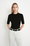 A model wearing the Rue Sophie Chabot Mock Neck Top in black, highlighting the fitted silhouette, structured shoulders, and clean mock neckline, front view.
