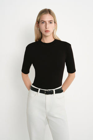 A model wearing the Rue Sophie Chabot Mock Neck Top in black, highlighting the fitted silhouette, structured shoulders, and clean mock neckline, front view.